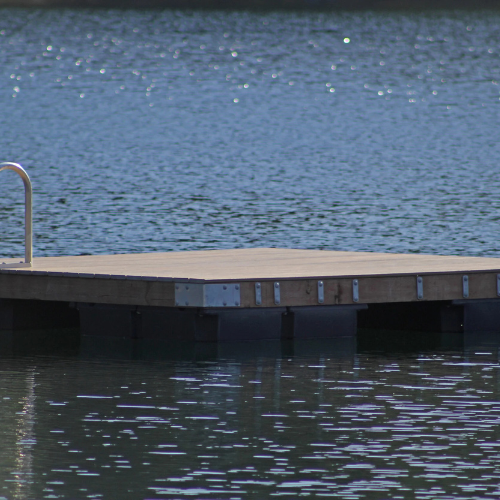A serene lake with a wooden dock and metal ladder extends into shimmering blue water, conveying a peaceful, inviting atmosphere ideal for relaxation.